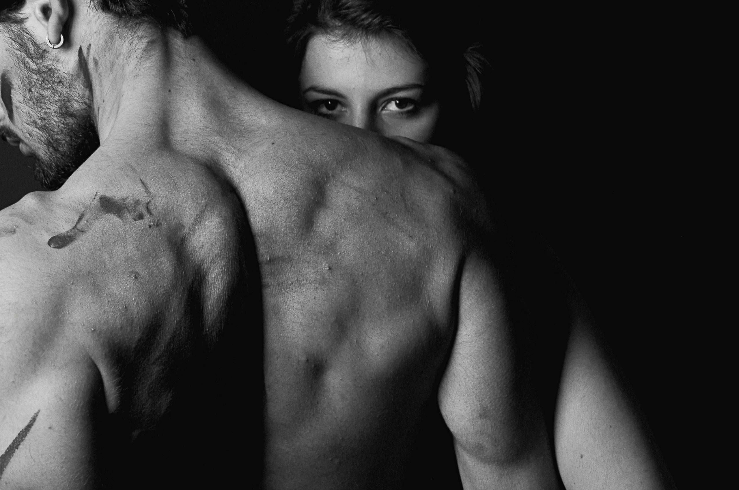 Black‑and‑white close‑up of two bare backs pressed together in shadow, highlighting muscular shoulders and soft curves as a visual metaphor for integrating masculine structure and feminine sensitivity in leadership.