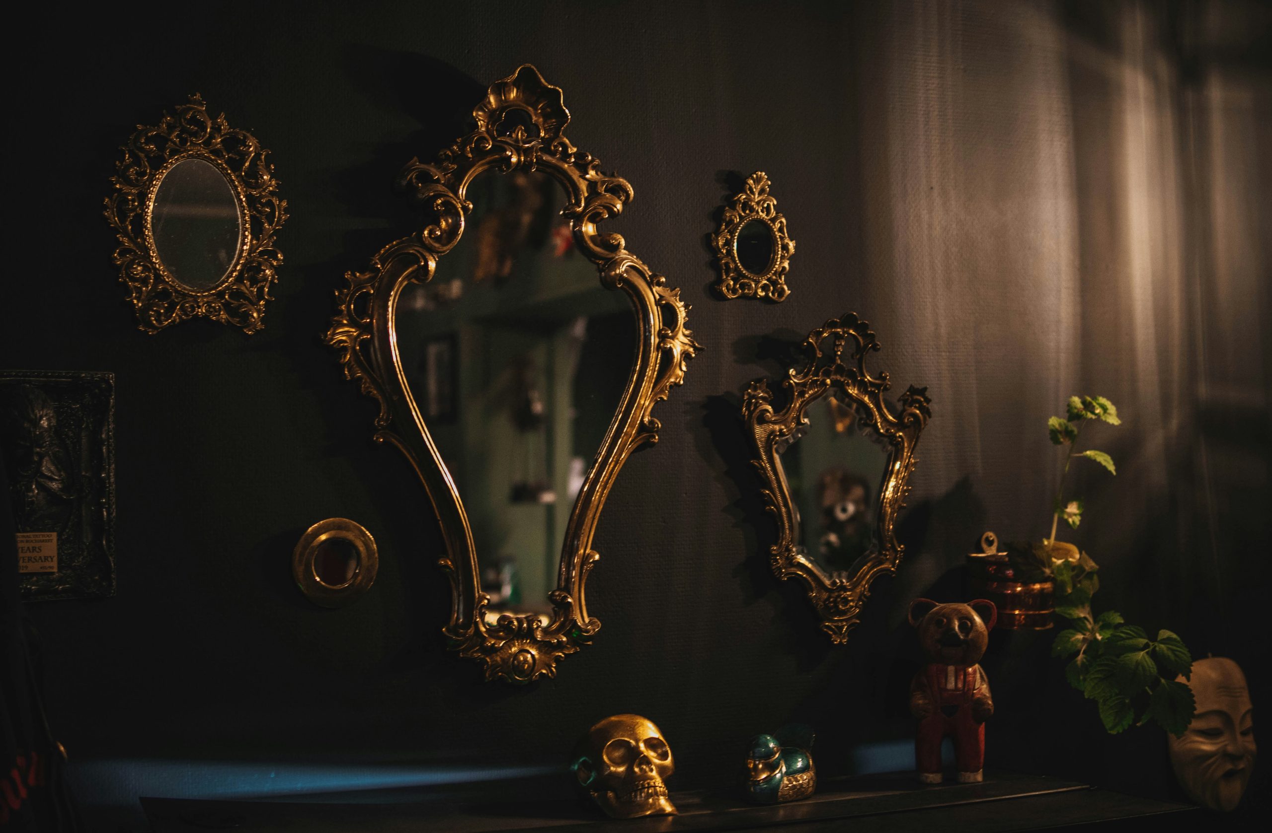 Ornate gold framed mirrors on a dark wall in a moody room, vintage mirror gallery reflecting cozy interior decor, symbolic business mirror concept for self reflection and nervous system work