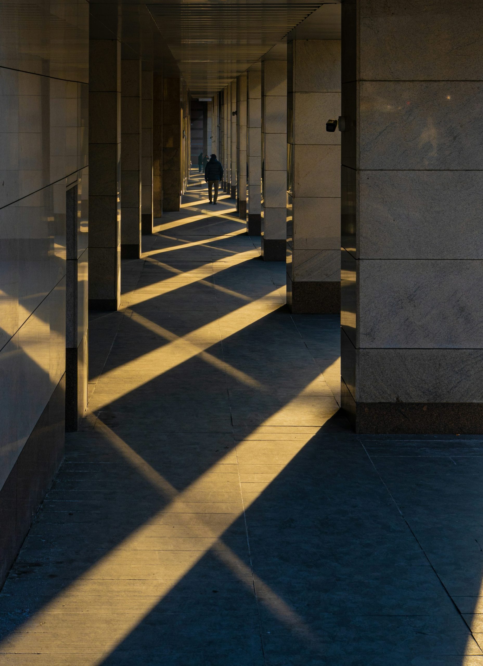 Person walking through an architectural corridor of light and shadow, representing AI visibility and the human experience of being seen.